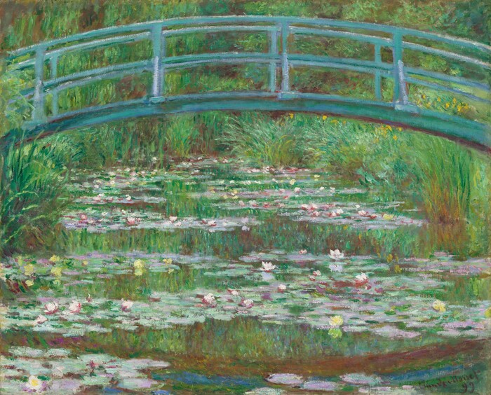 A green arched footbridge over a pond crowded with water lilies.